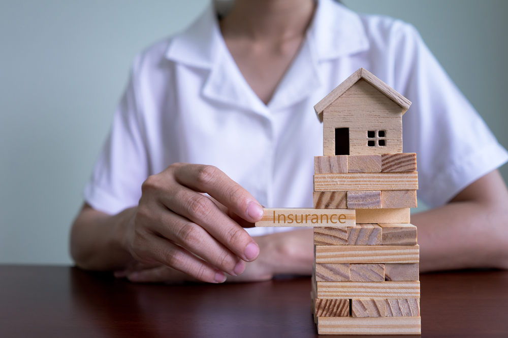 Insurance Agent Woman's hand stacking wooden blocks on a tower with house model